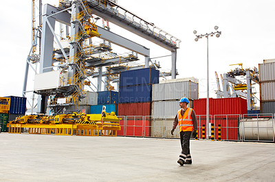 Buy stock photo Shot of a young man in workwear walking outside on a large commercial dock