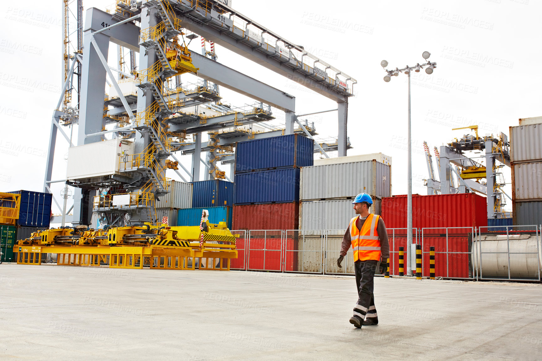 Buy stock photo Shot of a young man in workwear walking outside on a large commercial dock