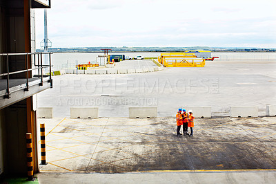 Buy stock photo High angle shot of three workers talking together while standing on a commercial dock