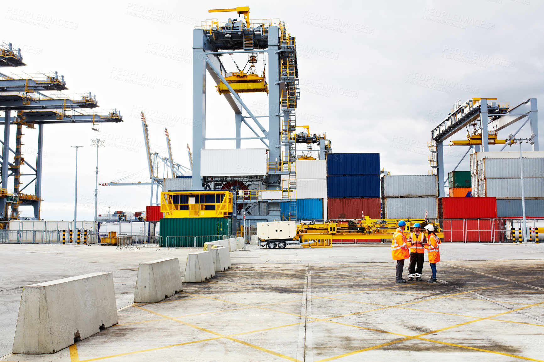 Buy stock photo High angle shot of three workers talking together while standing on a commercial dock