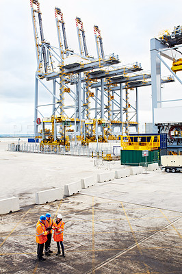 Buy stock photo High angle shot of three workers talking together while standing on a commercial dock