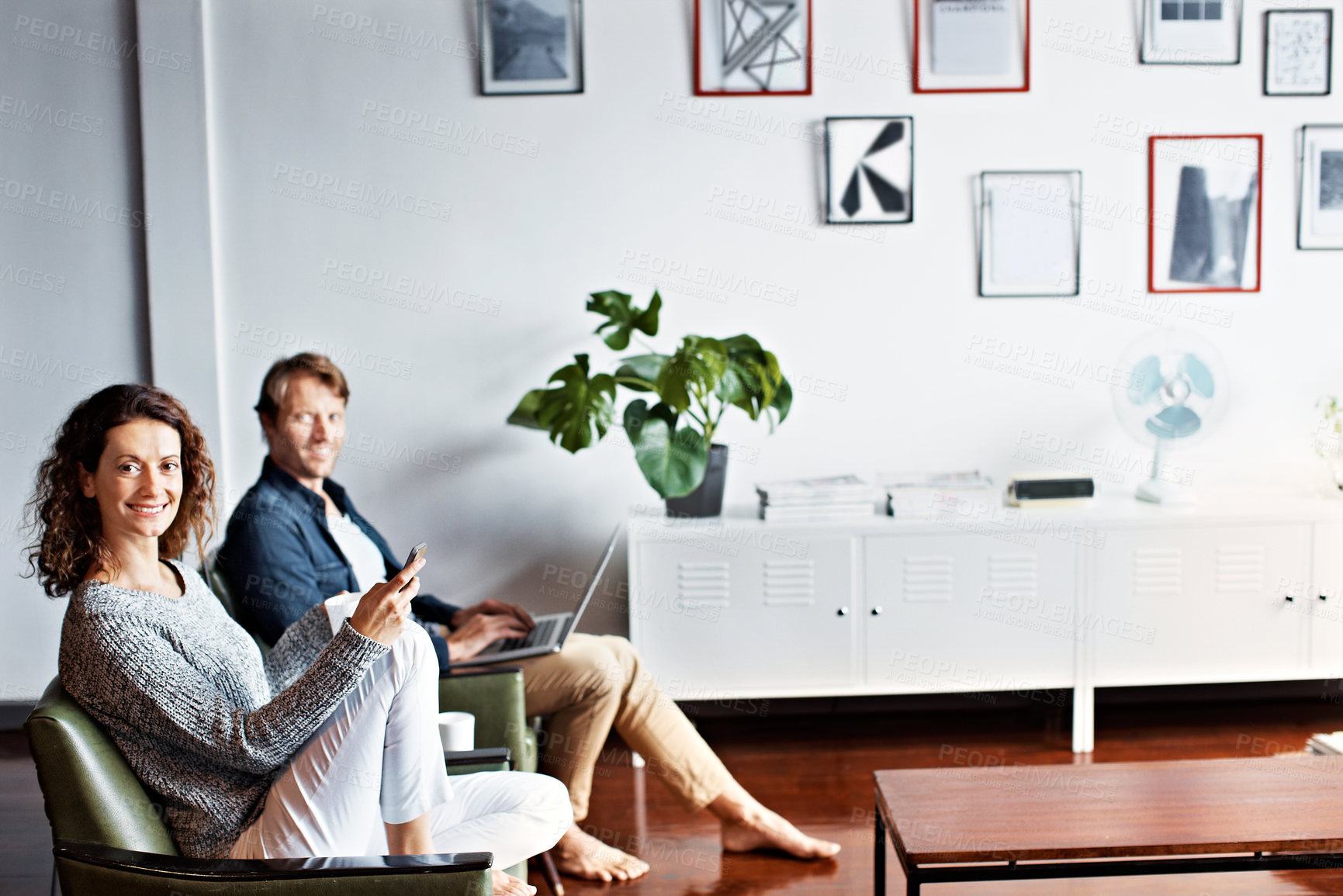 Buy stock photo Shot of a content mature couple sitting in their living room using a cellphone and using a laptop