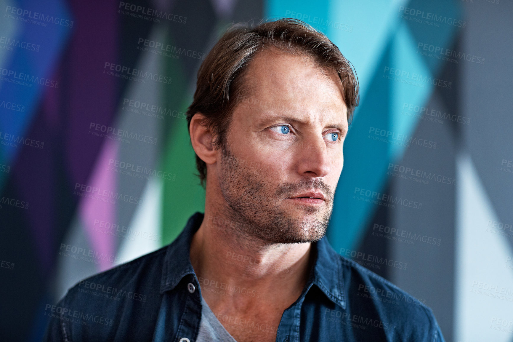 Buy stock photo Shot of a serious looking man standing in front of a colorful background