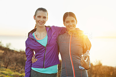 Buy stock photo Portrait of two smiling young friends standing arm in arm while out for a run
