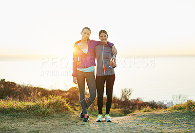 Buy stock photo Portrait of two smiling young friends standing arm in arm while out for a run