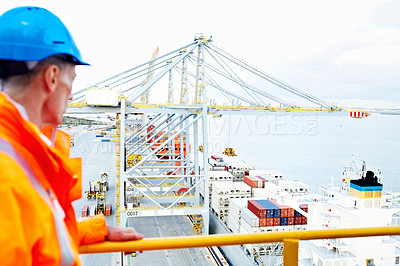 Buy stock photo Shot of a man in workwear standing on a walkway looking out over at a large commercial dock