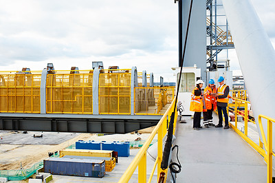 Buy stock photo Shot of three workers talking together while standing on an overhead walkway on a commercial dock