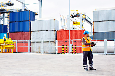 Buy stock photo Shot of a young man in workwear using a digital tablet while standing on a large commercial dock