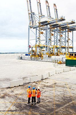 Buy stock photo High angle shot of three workers talking together while standing on a commercial dock