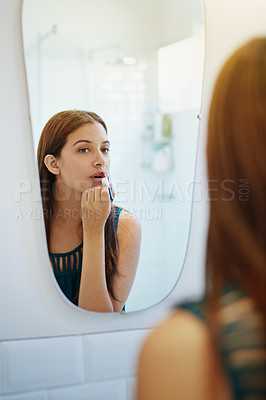 Buy stock photo Shot of a young woman putting on lipstick in her bathroom mirror