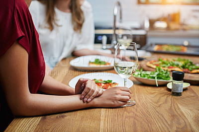 Buy stock photo Cropped shot of two friends sitting at the kitchen table eating pizza and drinking wine