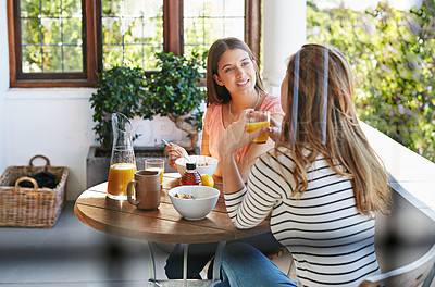 Buy stock photo Shot of two friends eating breakfast together on a balcony