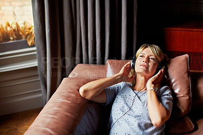 Buy stock photo Shot of a mature woman lying back on her sofa listening to music on headphones