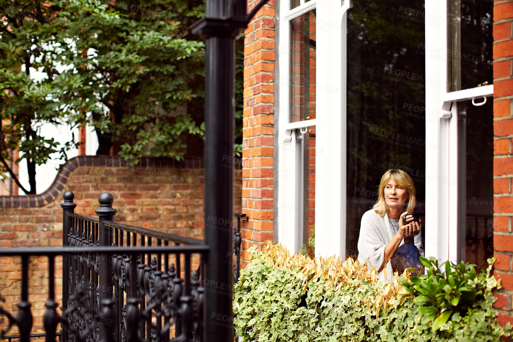Buy stock photo Shot of a mature woman drinking coffee while looking out of her window