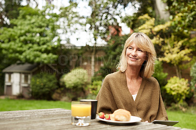 Buy stock photo Shot of a mature woman sitting in her yard eating breakfast