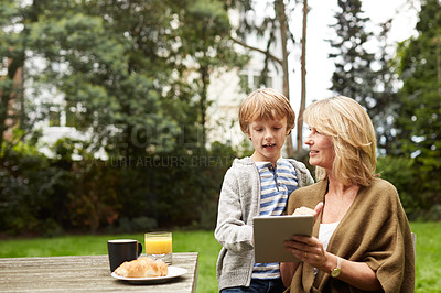 Buy stock photo Shot of a grandmother and her grandson sitting at a table in her yard using a digital tablet