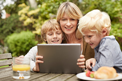 Buy stock photo Shot of a grandmother and her grandsons sitting at a table in her yard using a digital tablet