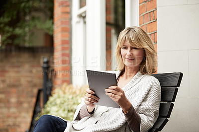 Buy stock photo Shot of a mature woman sitting on her front porch using a digital tablet
