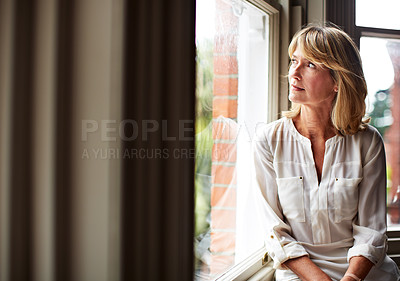 Buy stock photo Shot of a mature woman sitting by a window at home