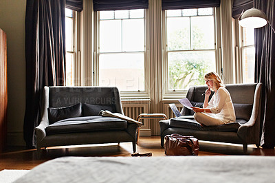 Buy stock photo Shot of a mature woman working on a laptop and reading paperwork in her living room after a trip