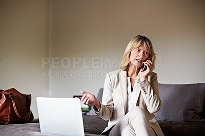 Buy stock photo Shot of a mature businesswoman sitting on a hotel bed using a laptop and talking on the phone