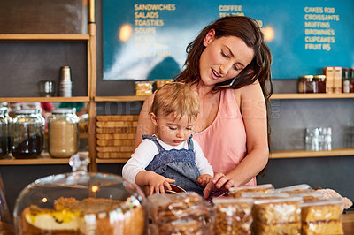 Buy stock photo Shot of a woman talking on the phone in a bakery with her little girl next to her on the counter