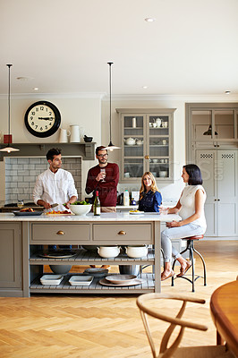 Buy stock photo Shot of a group of friends talking and drinking wine together while preparing dinner