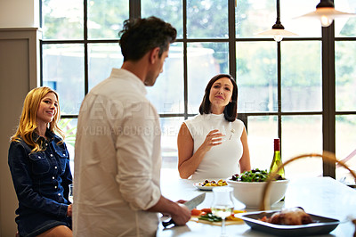 Buy stock photo Shot of a group of friends talking and drinking wine together while preparing dinner