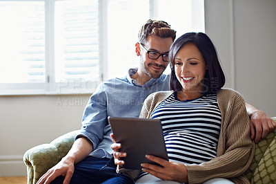 Buy stock photo Shot of a pregnant woman and her husband sitting on thier sofa using a digital tablet