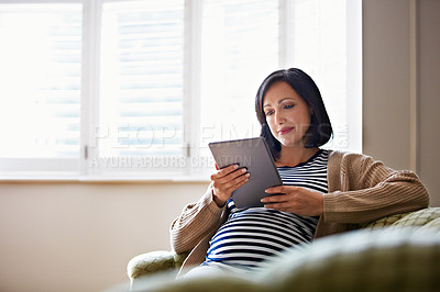 Buy stock photo Shot of a pregnant woman sitting on her sofa using a digital tablet