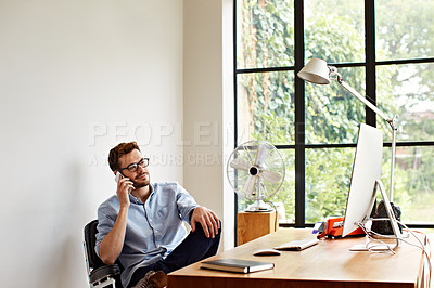 Buy stock photo Shot of a young man talking on the phone while working in his home office