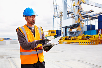 Buy stock photo Shot of a young man in workwear going through paperwork while standing on a dock