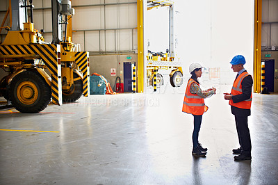 Buy stock photo Shot of two warehouse workers talking together inside of a large warehouse