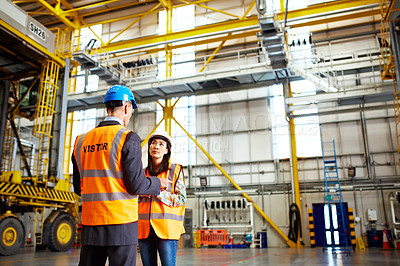 Buy stock photo Shot of two warehouse workers talking together inside of a large warehouse