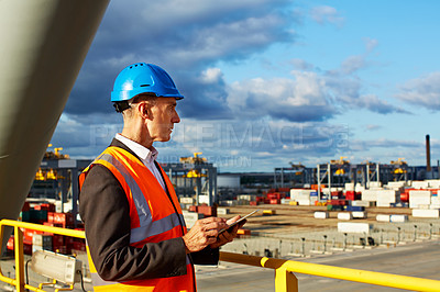 Buy stock photo Shot of a man in workwear standing on a walkway looking out over at a large commercial dock