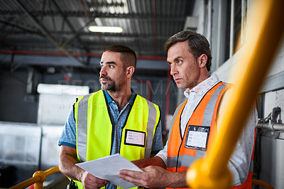 Buy stock photo Shot of two warehouse workers standing on stairs discussing papework