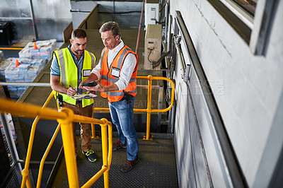 Buy stock photo Shot of two warehouse workers standing on stairs discussing papework
