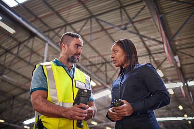 Buy stock photo Shot of two coworkers talking together over a barcode reader while standing in a large warehouse