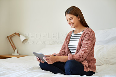 Buy stock photo Shot of a young woman sitting on her bed using a digital tablet