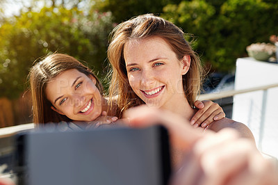 Buy stock photo Shot of two friends taking a selfie together while standing outside
