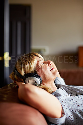 Buy stock photo Shot of a mature woman sitting back on her sofa listening to music on headphones
