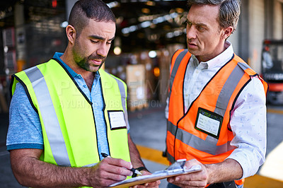 Buy stock photo Shot of two workers talking together over a clipboard inside of a warehouse