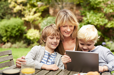 Buy stock photo Shot of a grandmother and her grandsons sitting at a table in her yard using a digital tablet