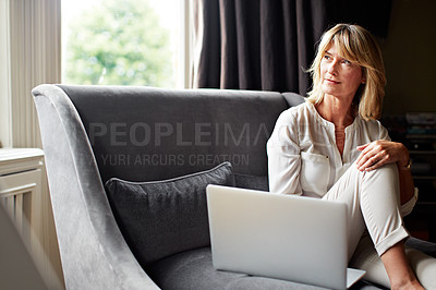 Buy stock photo Shot of a mature woman sitting on her sofa using a laptop