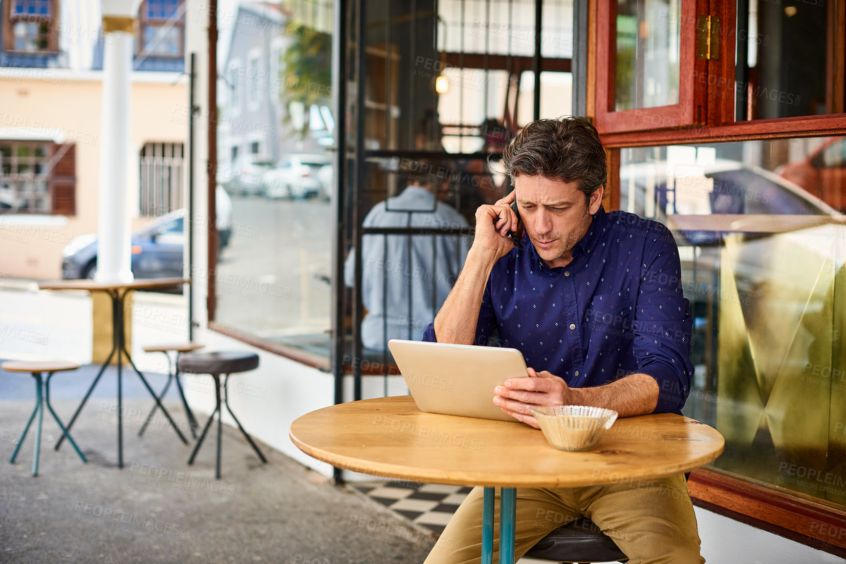 Buy stock photo Shot of a mature man sitting on patio table at a cafe using a tablet and cellphone