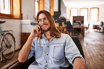 Buy stock photo Shot of a young designer talking on his phone while sitting in an office