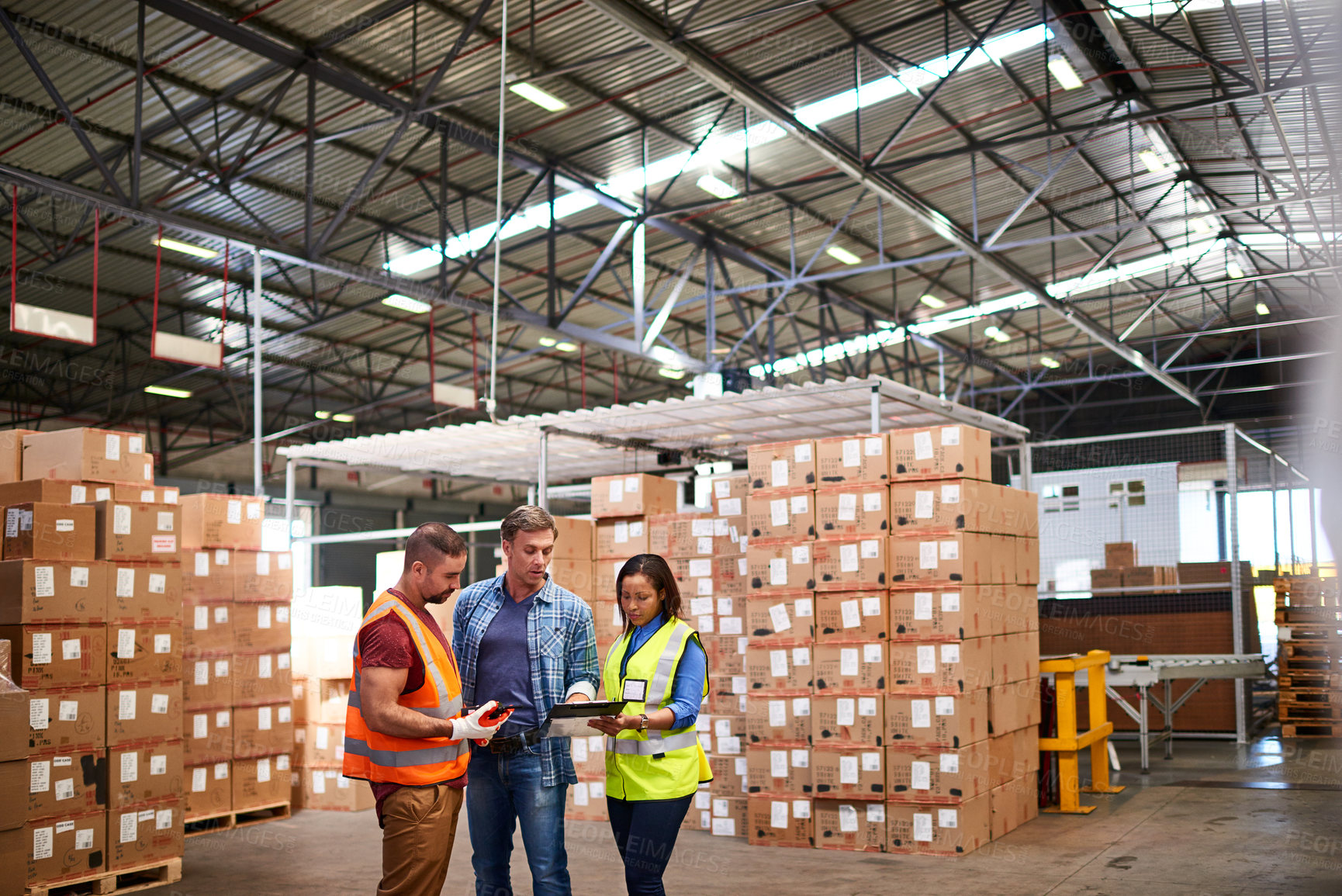 Buy stock photo Shot of a group of coworkers talking together while standing in a large warehouse full of boxes