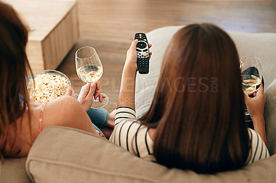 Buy stock photo Rearview shot of two friends sitting on a sofa drinking wine and watching a movie on tv