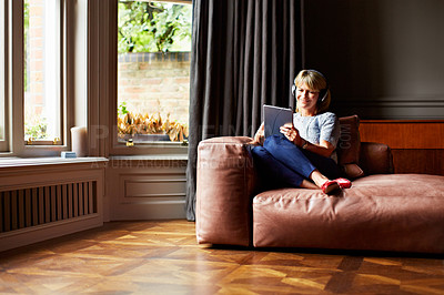 Buy stock photo Shot of a mature woman sitting on her sofa using a digital tablet