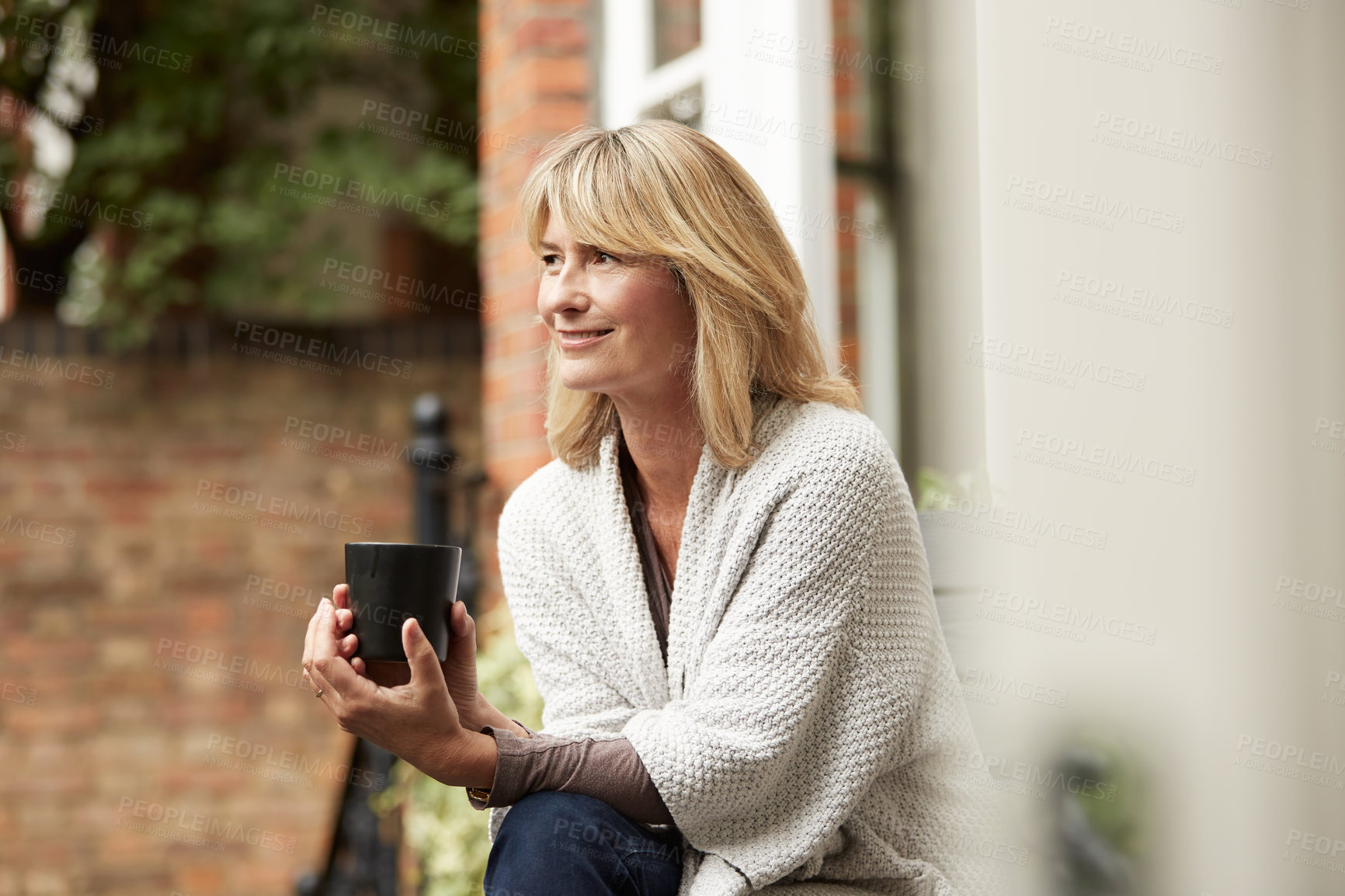 Buy stock photo Shot of a mature woman leaning against the railing of her front porch drinking a coffee